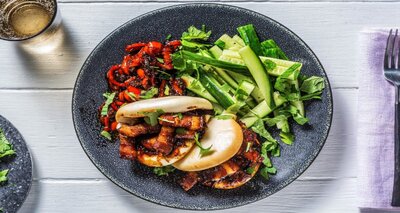 Gestoomde bao bun met speklap in ketjapmarinade met rode puntpaprika, zoetzure komkommer en munt